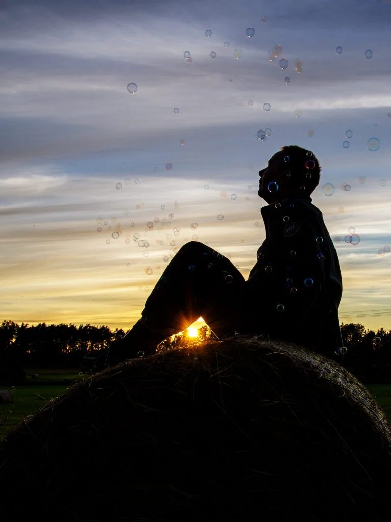 Heinapallil istuva mehe siluett päikeseloojangu paistel